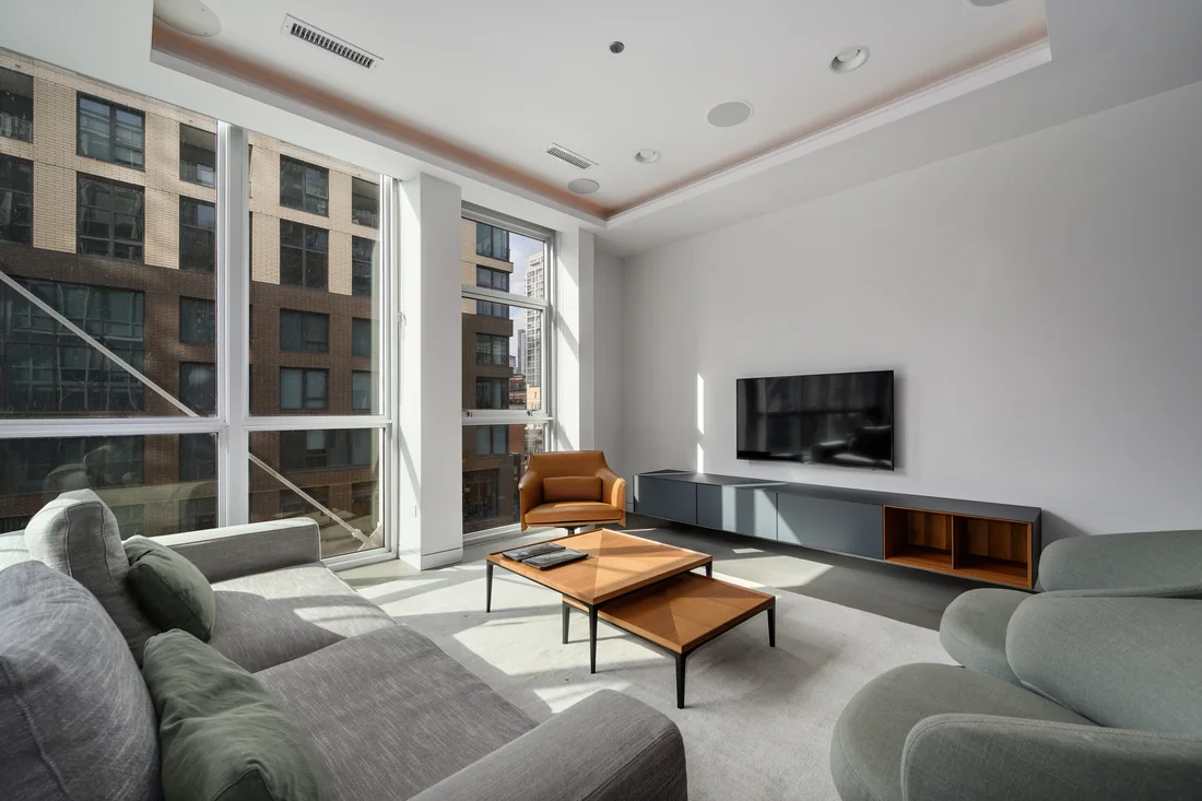Sunlit living room with tall windows, gray seating and warm leather accents