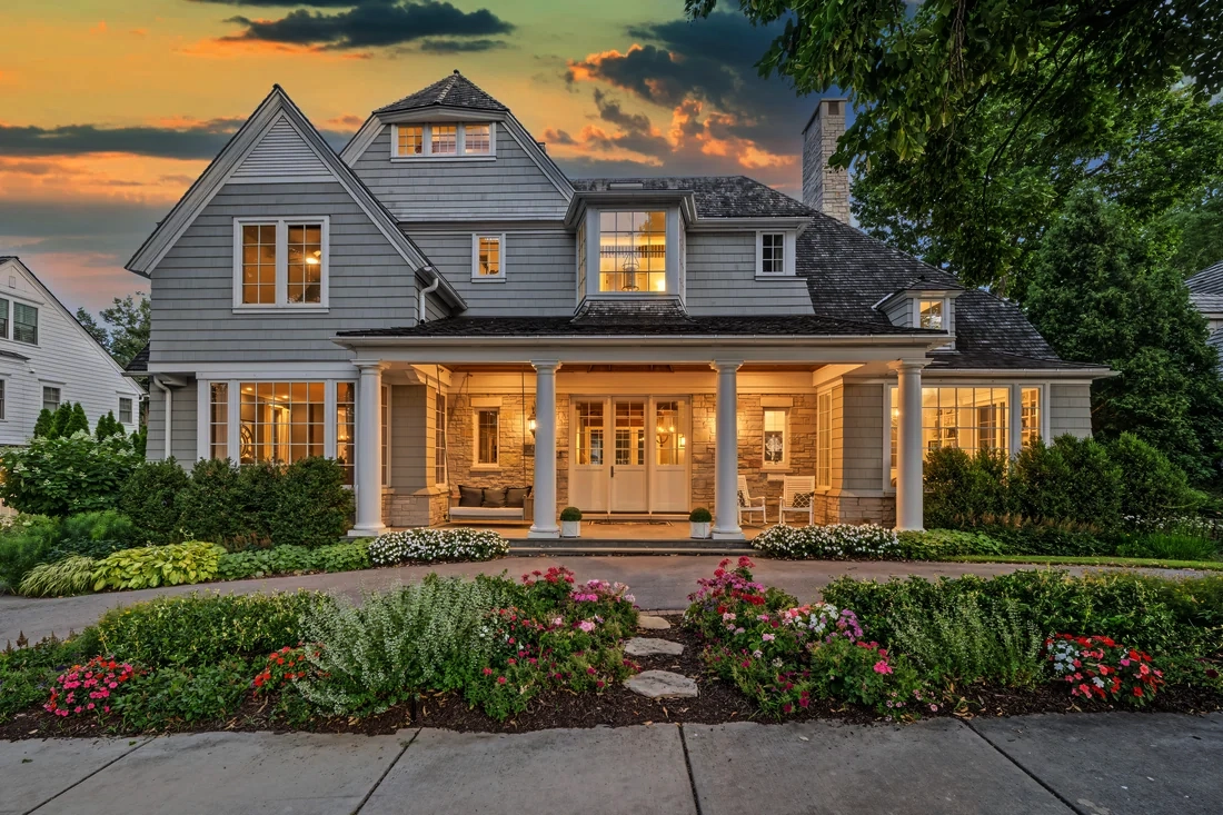 Gray gabled home with a warmly illuminated porch beneath an evening sky