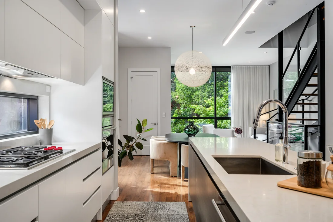 Modern kitchen with pale cabinetry, wood floors and views into a tree-facing dining area