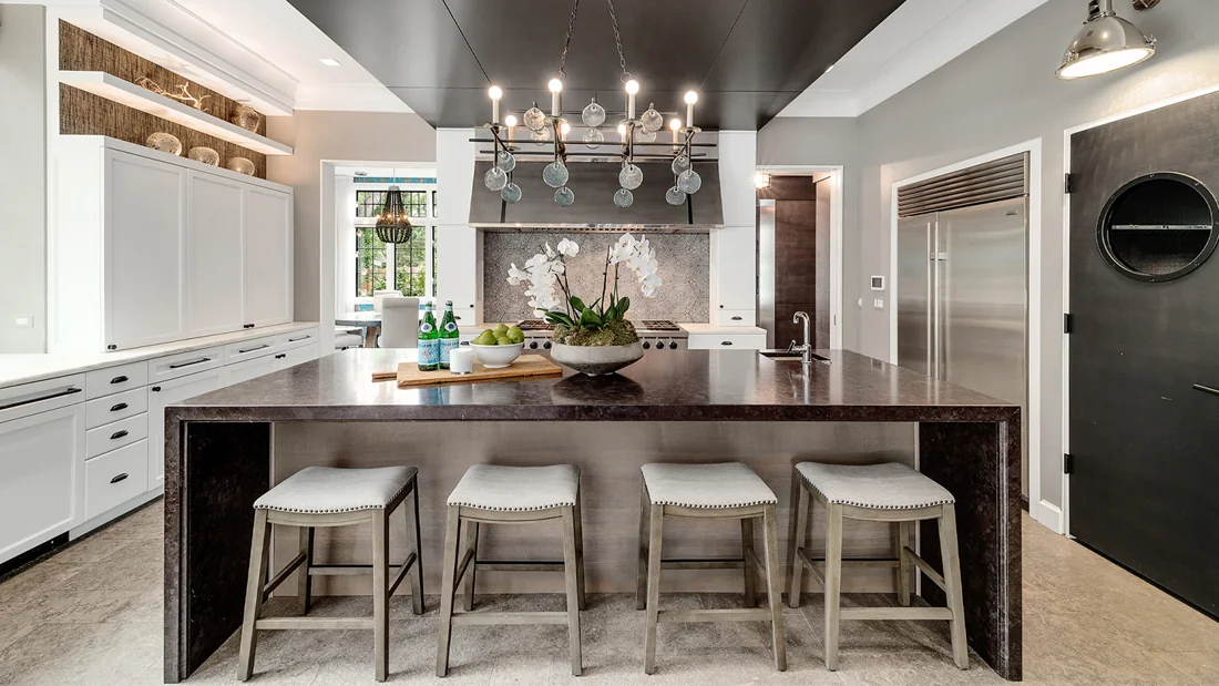 White kitchen with a dark ceiling, island seating and sculptural chandelier