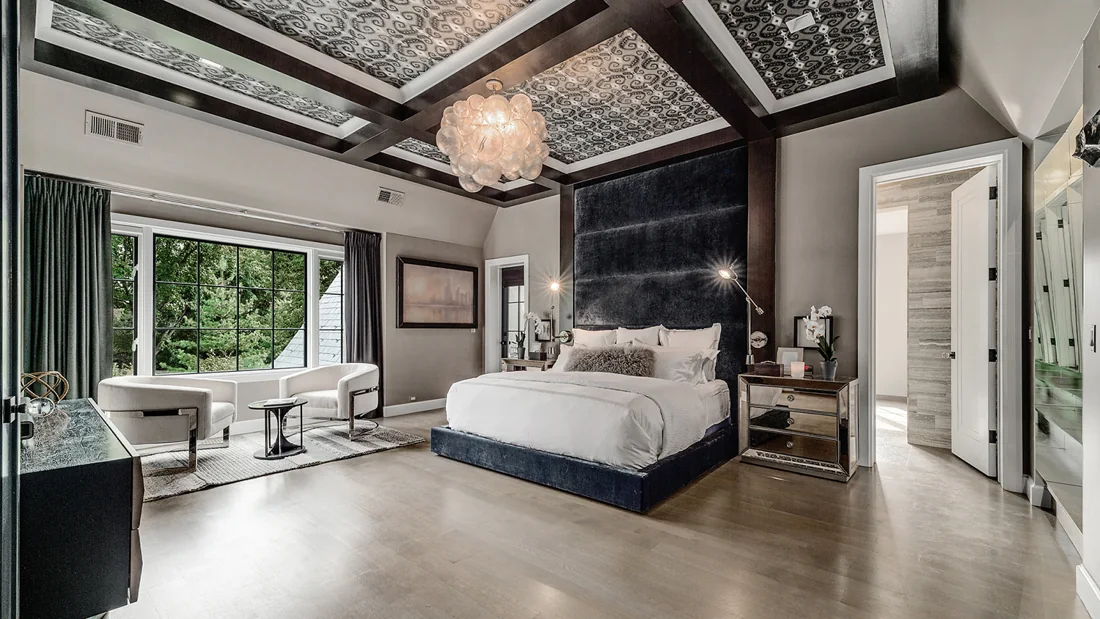 Spacious bedroom with patterned ceiling, chandelier and garden views